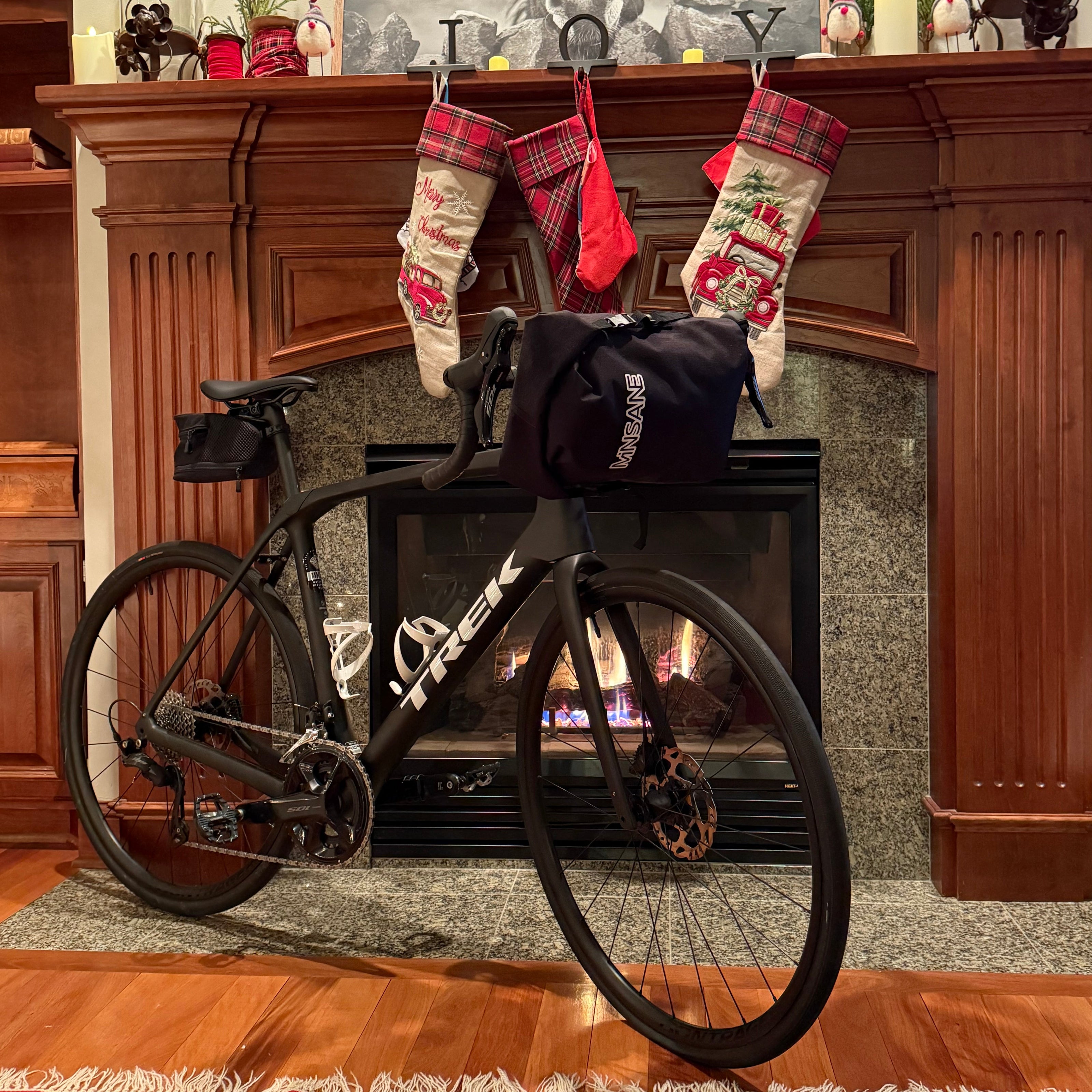 Full carbon gravel bike in front of fireplace with a fully loaded front attached to the handlebar.